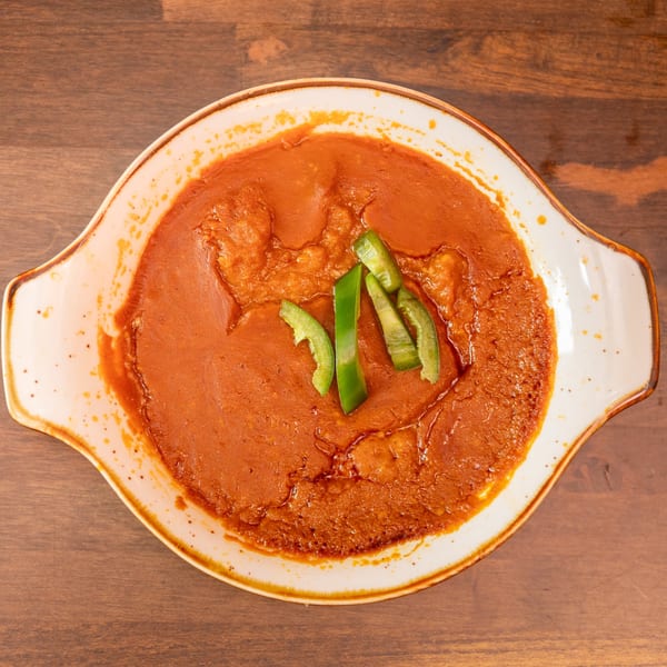 Red saucy dish with green bell pepper slices in a white serving dish on a wooden table.