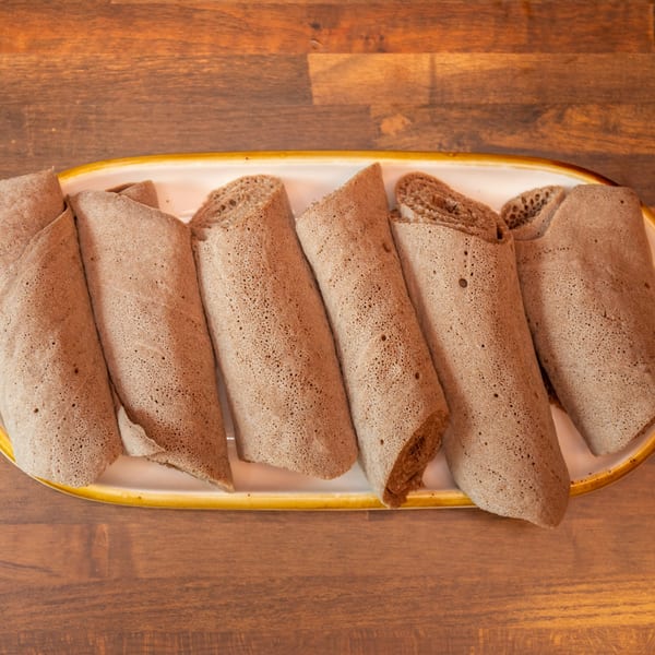 Rolled injera bread pieces on a white platter with a yellow rim on a wooden table.