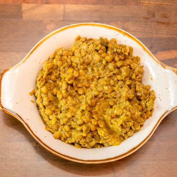 Hearty yellow lentil stew in a white serving dish on a rustic wooden surface.