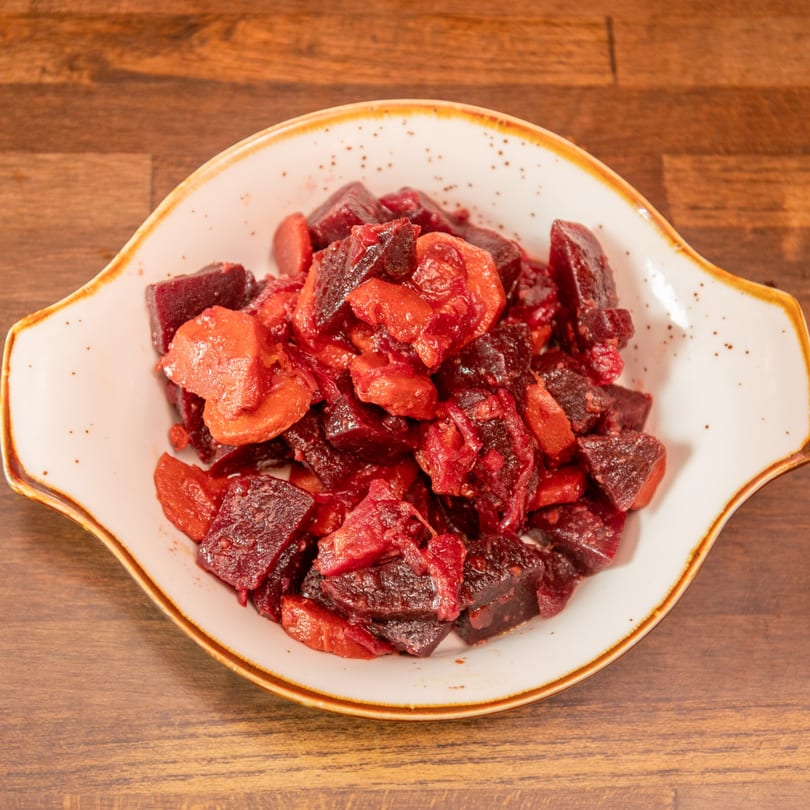 Diced beets and carrots in a white bowl on a wooden table.