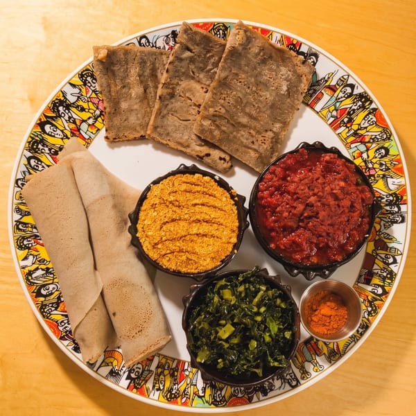 A colorful plate with injera bread, three bowls of different Ethiopian dishes, and a small cup of spice.