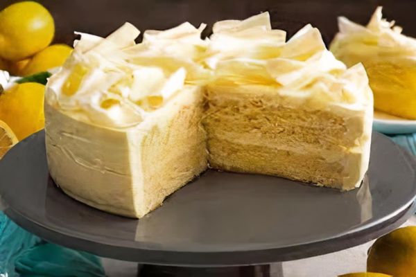 Delicious lemon mascarpone cake with creamy layers, topped with white chocolate curls, displayed on a cake stand.