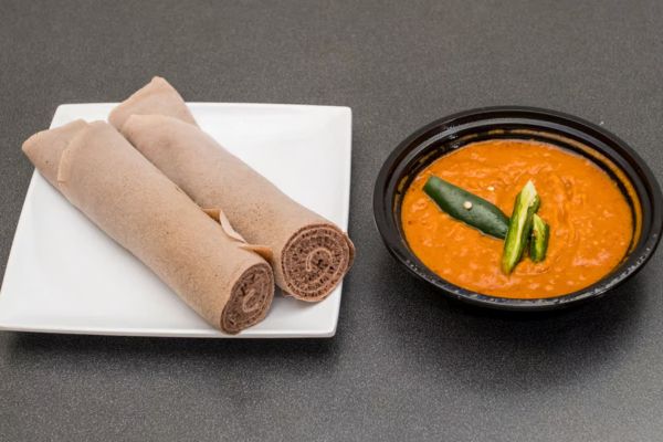 Ethiopian shiro wat, a spiced chickpea stew, served with rolled injera and garnished with green chili.