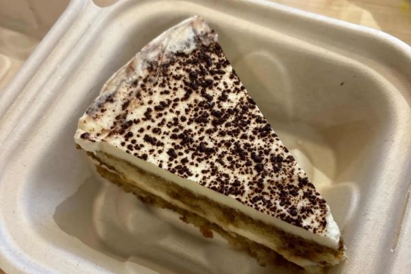 A slice of creamy tiramisu topped with cocoa powder, served in an eco-friendly takeout container.